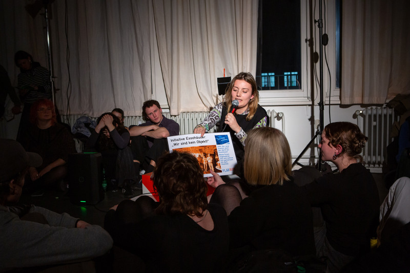 Lisa Zander spricht zum Publikum und hält ein großes Foto hoch.